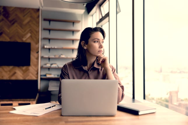 woman at desk staring out window shutterstock_2022462290